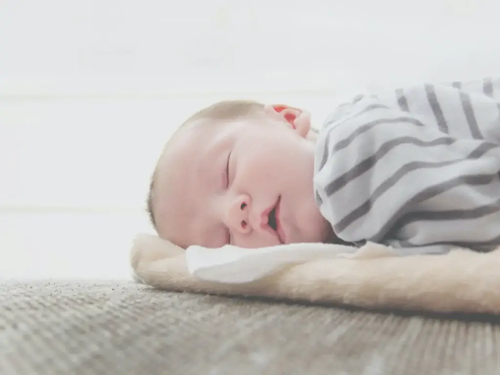 Sleeping newborn resting on a light carpet with a gray striped blanket partially covering them