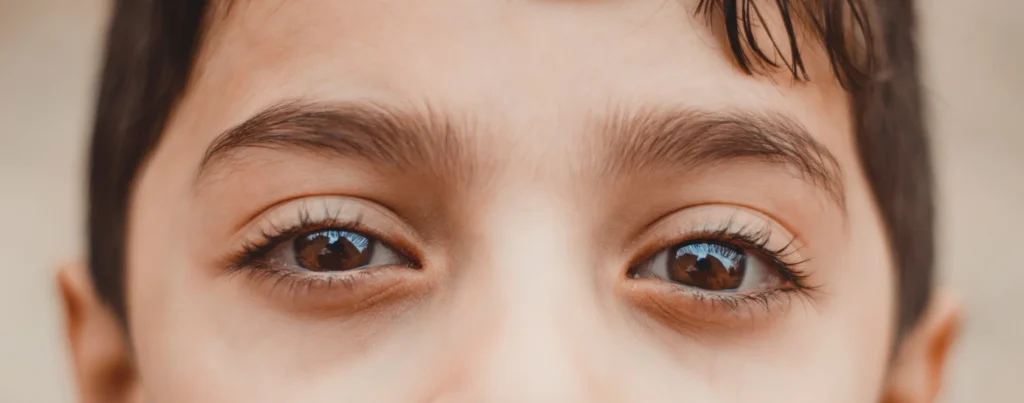 Close-up of a young boy's brown eyes, looking slightly upward, with soft lighting and long lashes.