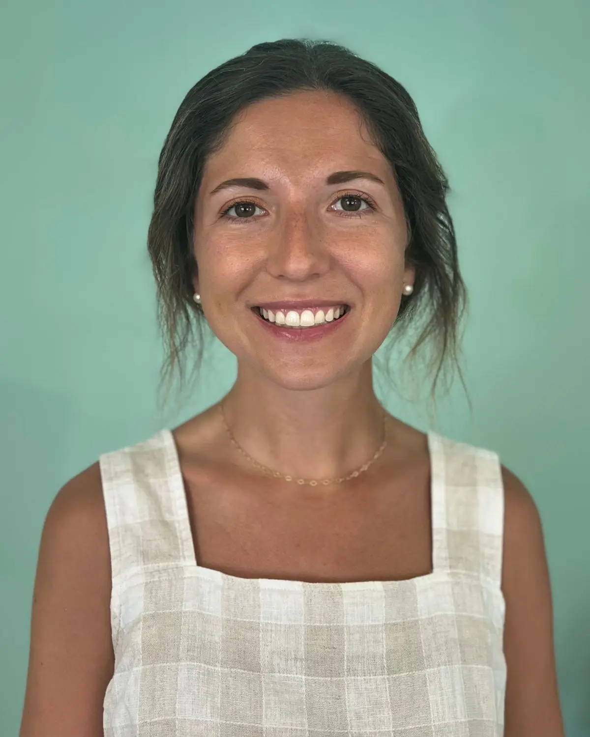 Young, smiling woman with an updo. Wearing a plaid/gingham shirt against a green background