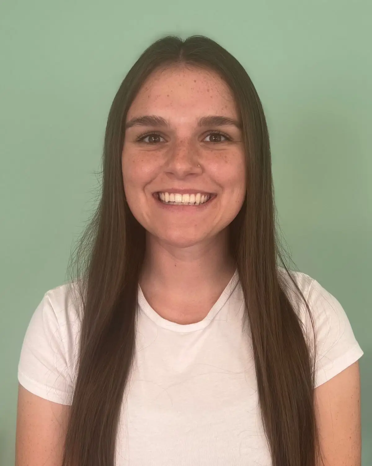 Image of a smiling young woman with long, brown hair wearing a white T-Shirt, against a green background